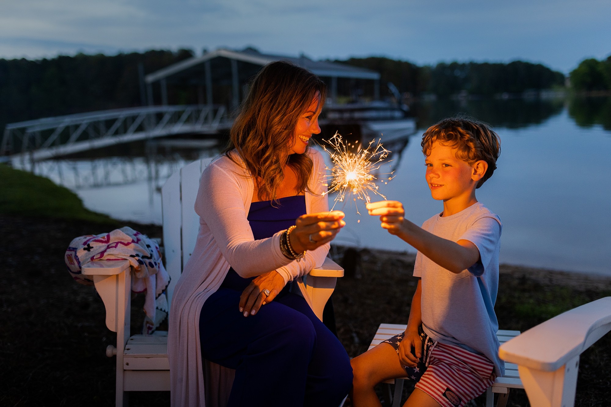 Mother and son watching fireworks at campfire at summer lake house.