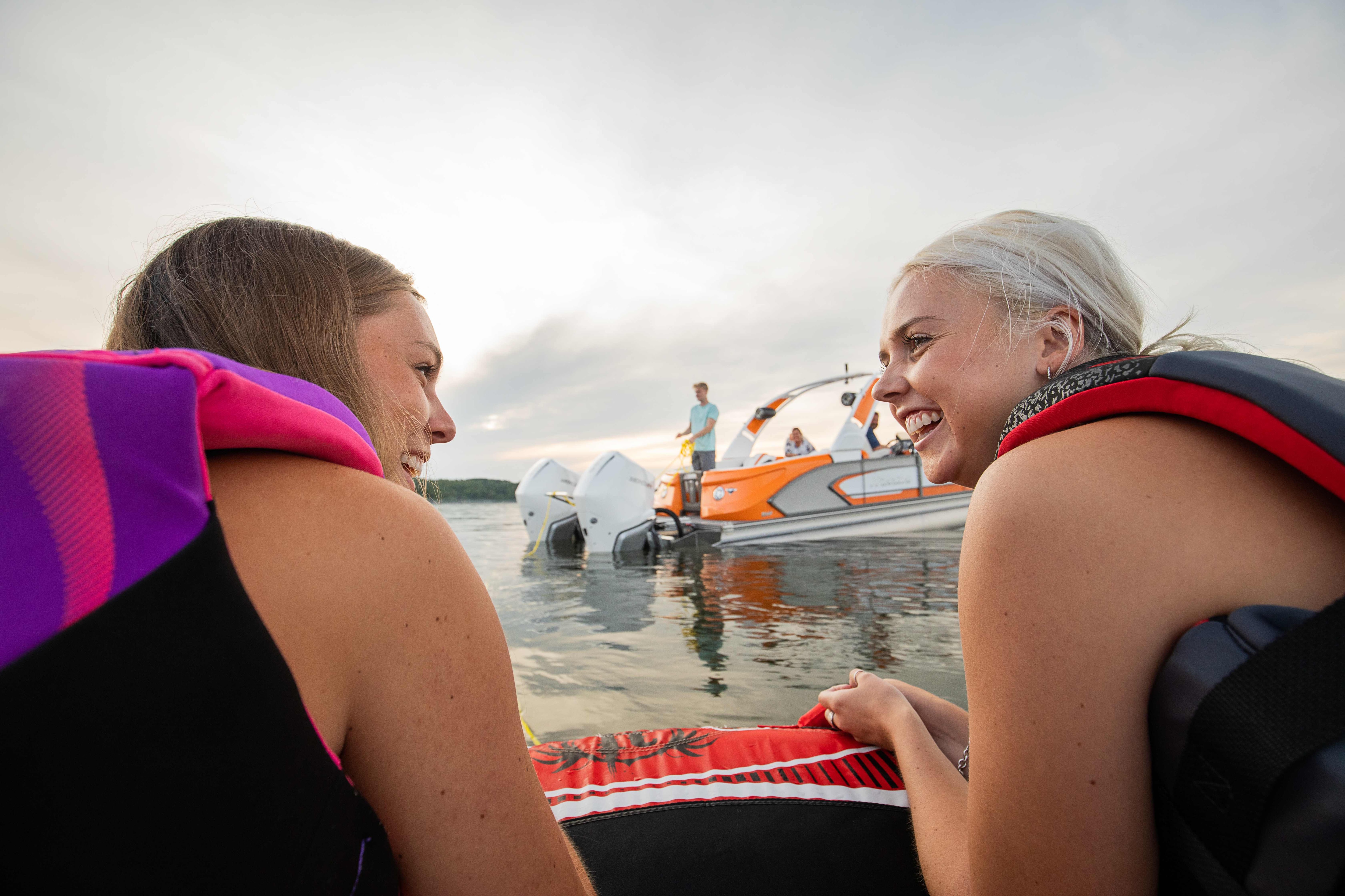 2 girls on a floating tube towing by a a Manitou LX pontoon boat