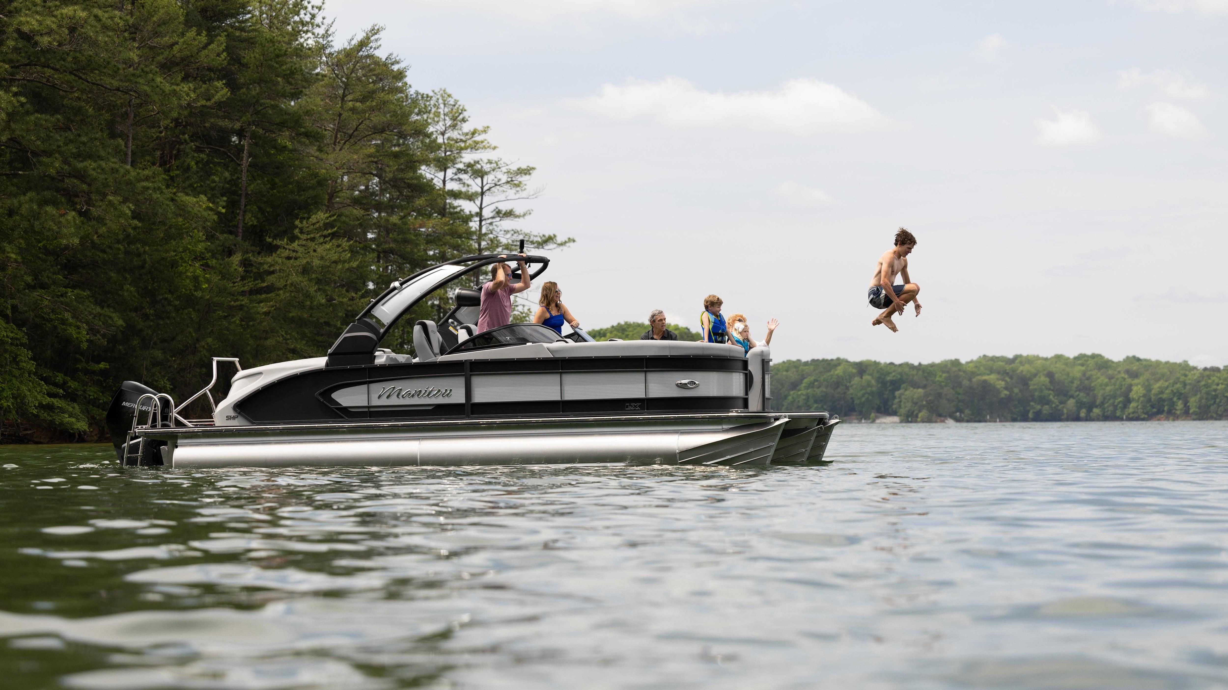 Boy jumping off Manitou LX into lake on Family Boating Trip