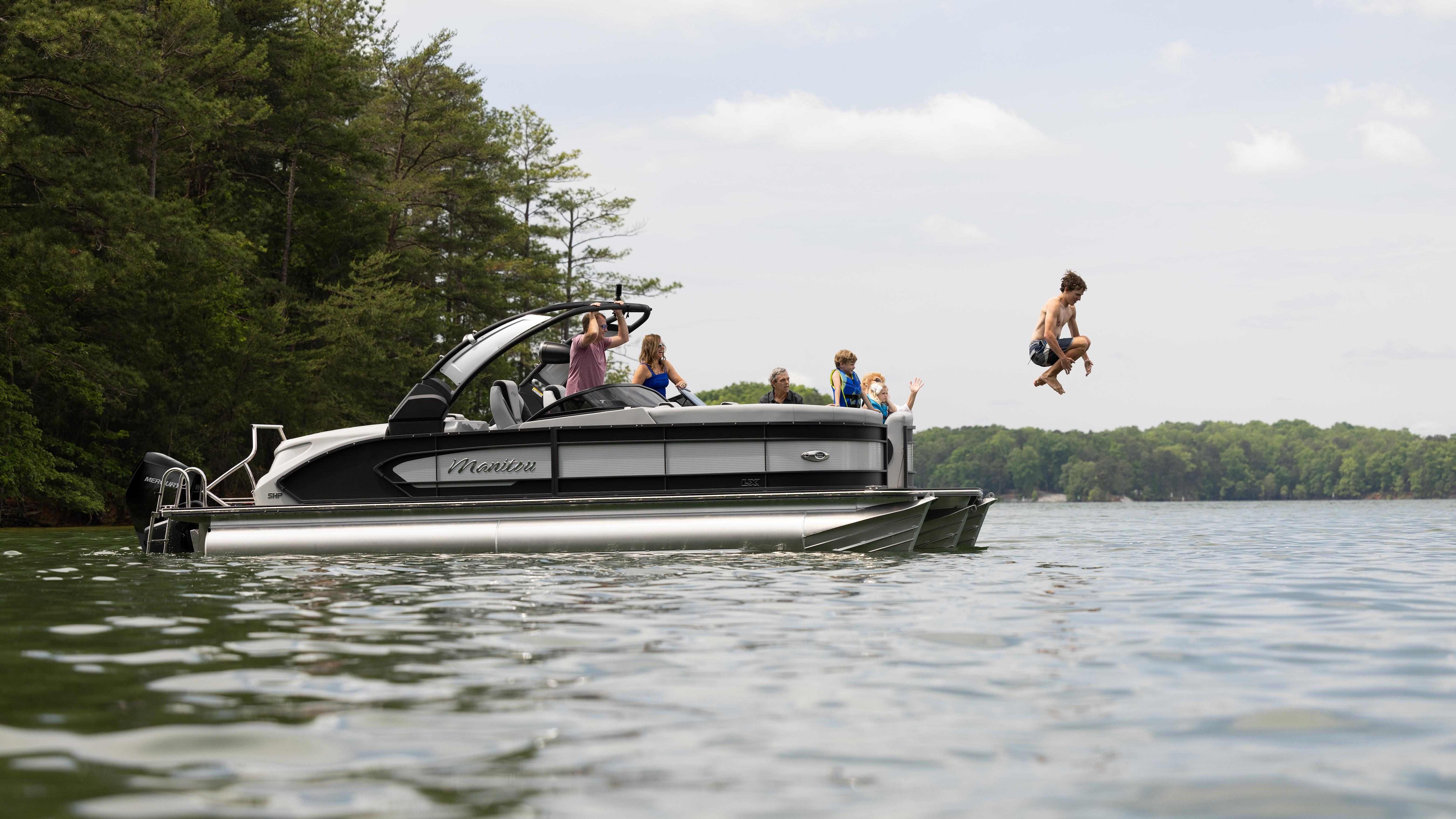 Boy jumping off Manitou LX into lake on Family Boating Trip