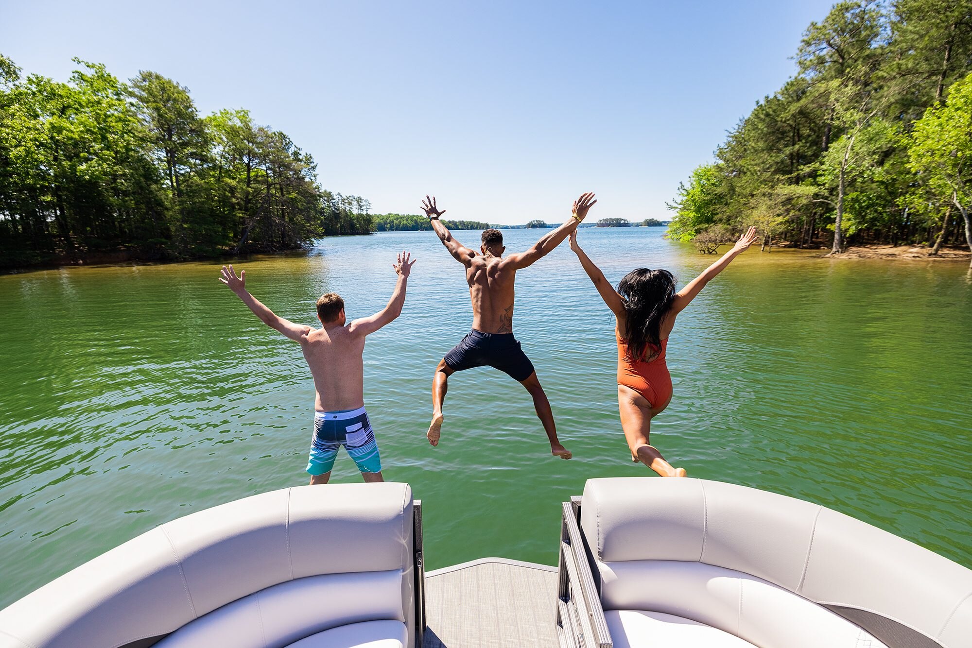 3 people jumping in the water from the Manitou Encore Pontoon Boat
