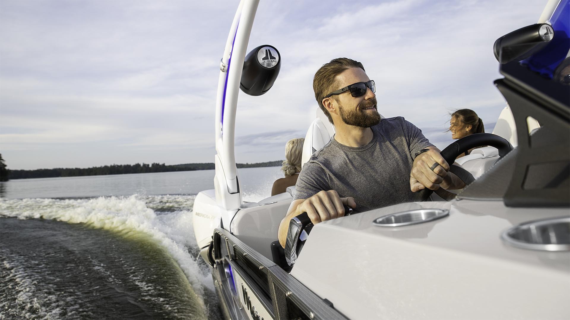 Homme conduisant son bateau ponton Manitou sur un lac
